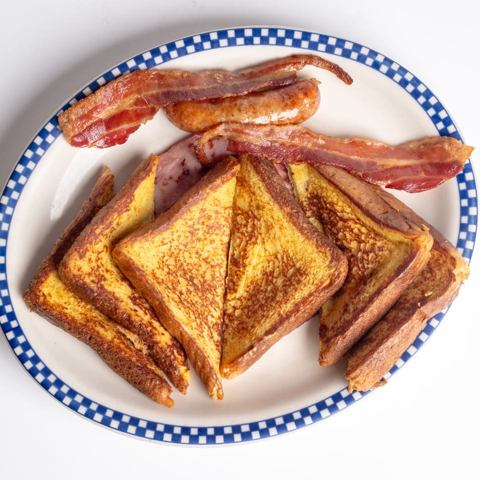 A diner breakfast plate with golden French toast, crispy bacon, and a sausage link.
