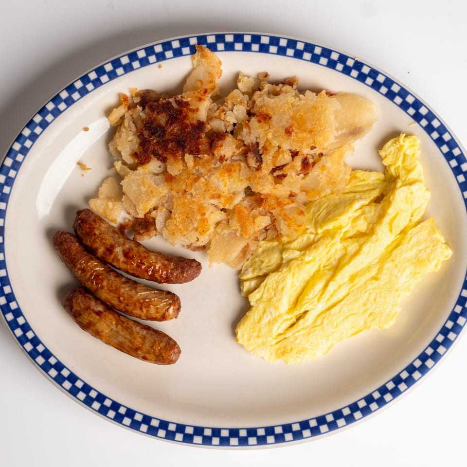 A diner breakfast plate with scrambled eggs, three sausage links, and crispy hash browns.