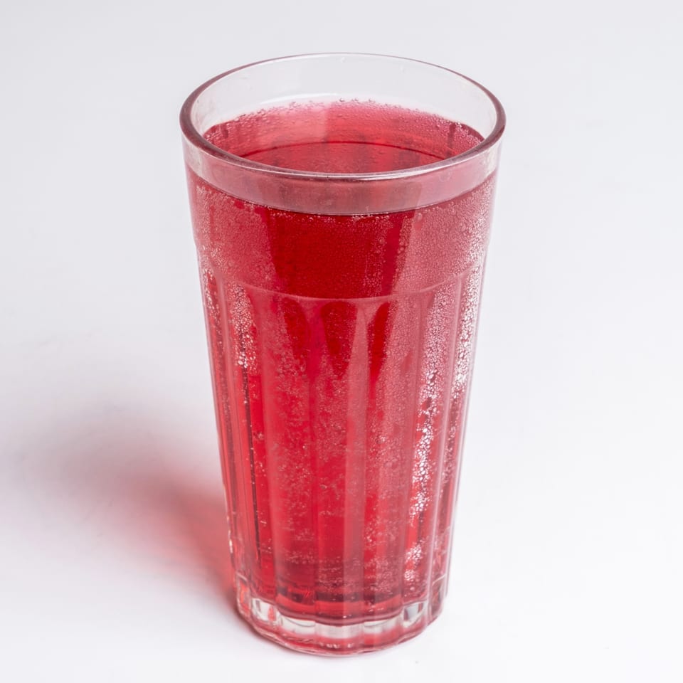 A tall glass of bubbly red soda, a classic diner beverage, on a white background.