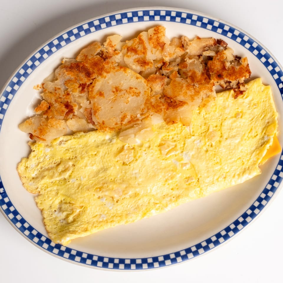 A diner breakfast plate with a golden omelet and crispy home fries on a blue and white checkered plate.