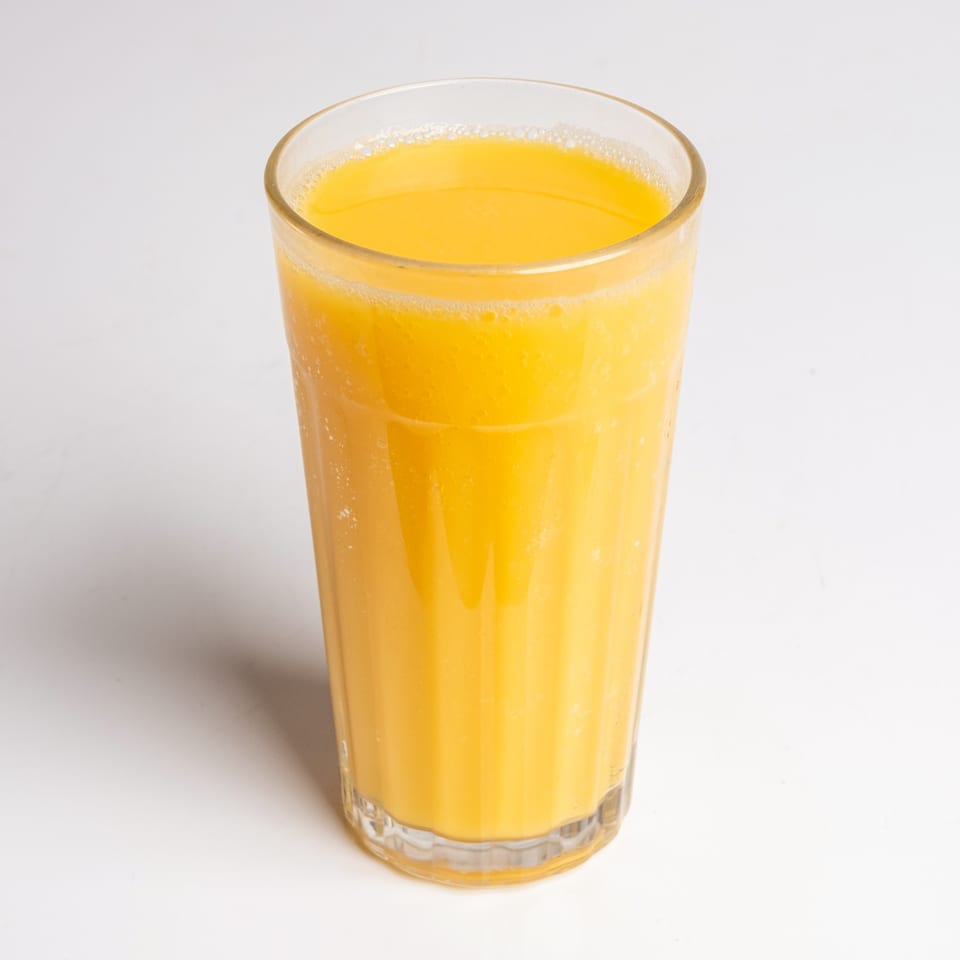 A tall glass of fresh orange juice with a foamy top, ready to drink at Sunny Side Diner.