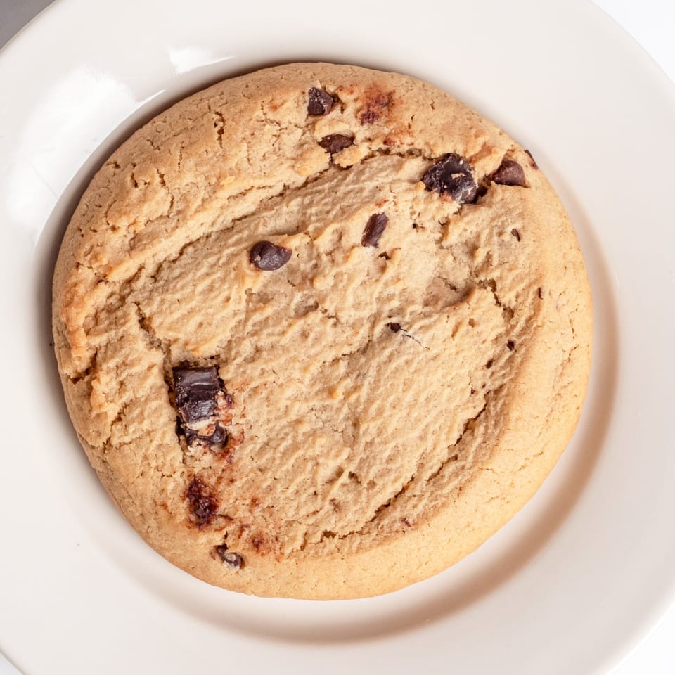 A large, round chocolate chip cookie with a crinkled surface, served on a white plate.